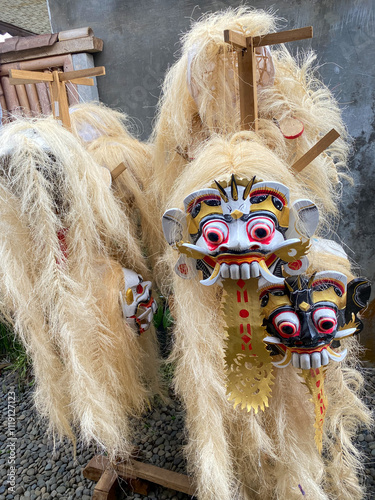 Bali, Indonesia - October 26, 2024: Several Balinese rangda masks, tapel rangda, leak masks of traditional dance with long white hair hang neatly on a wooden rack photo