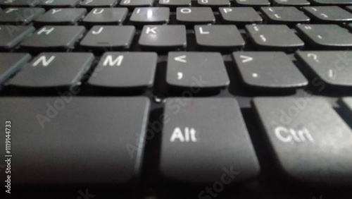 A minimalist, black laptop keyboard with clean, white keys, isolated on a wooden background.