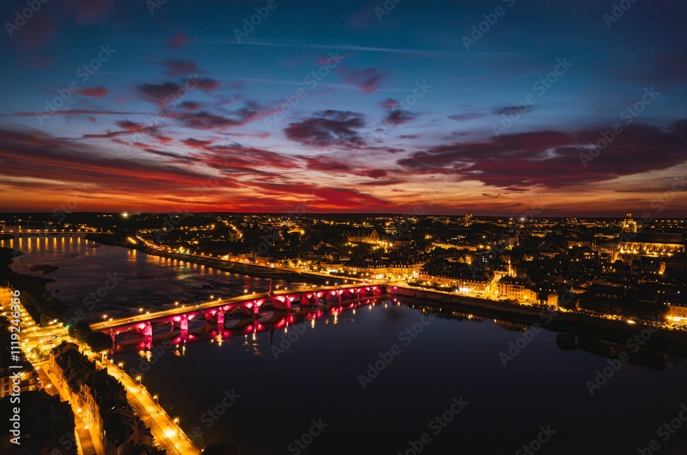 Obraz premium Colorful sunset casts a magical glow over the illuminated city and river at twilight