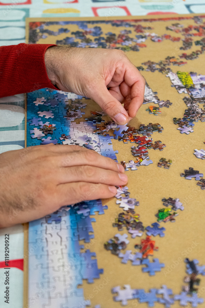 Hands of a man working on a puzzle at home, the man needs to clear and relax his mind with his favorite hobby. Hands of a man working on a puzzle at home, the man needs to clear and relax his mind with his favorite hobby.