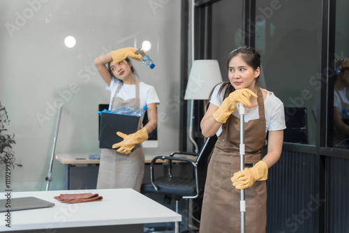 Two Asian housekeepers wear overalls and work together efficiently to clean the living room, study, office.They wipe the windows, mop the floors, inspect the shop to make sure the work is spotless photo