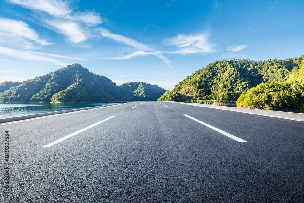 Asphalt road and lake water with green mountain natural landscape under blue sky. Outdoor natural background.