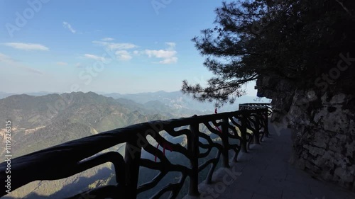 A narrow walkway carved into the side of a cliff, with a vast panoramic view of the forested valley and mountains in Jinxiu, Guangxi. Concept of travel, adventure, hiking in Southern China. photo