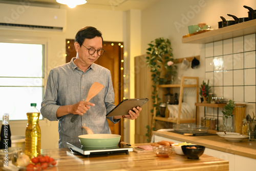 Portrait of senior man following a recipe on digital tablet while cooking in his home kitchen photo