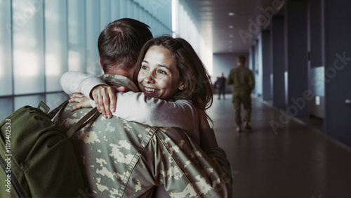 Joyful reunion in an airport hallway as a woman embraces her returning military partner.