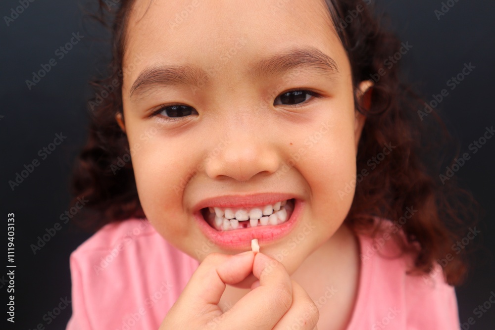 Asian female toddler smiling showing her missing tooth while holding her missing tooth close up. Asian female toddler smiling showing her missing tooth while holding her missing tooth close up.