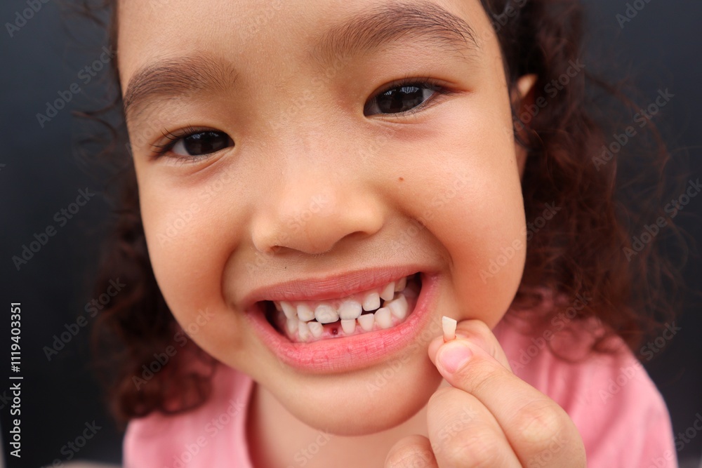 Asian female toddler smiling showing her missing tooth while holding her missing tooth close up. Asian female toddler smiling showing her missing tooth while holding her missing tooth close up.