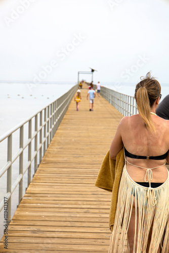 A woman dressed in a bikini is leisurely walking down a wooden pier