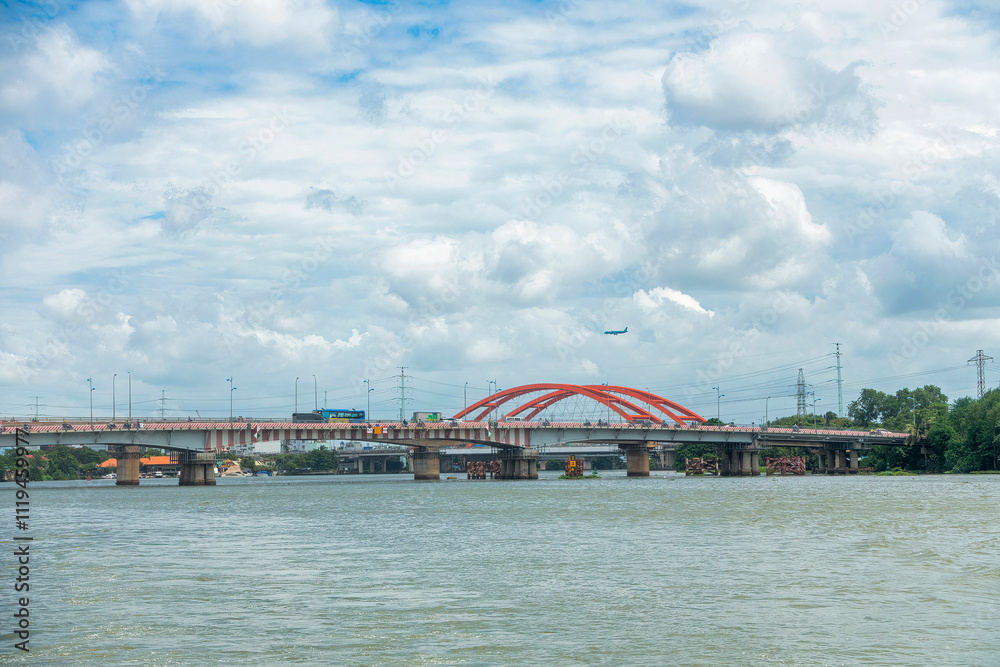 Fototapeta premium An airplane is flying over Binh Loi Bridge, Ho Chi Minh City, preparing to land at the airport.