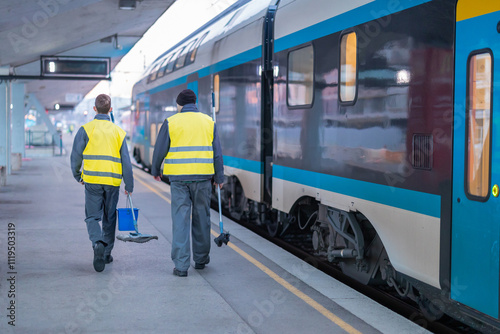 Two train cleaners with mop and bucket walking along the train on a station waiting to be cleaned. Early morning on ljubljana train station.