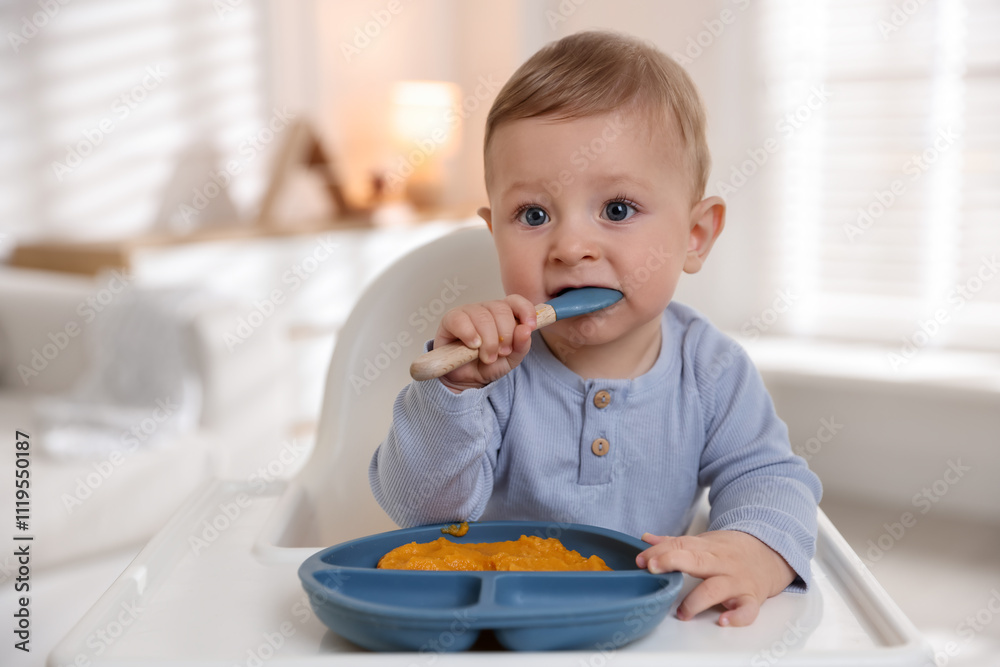 Cute little baby eating healthy food in high chair indoors Cute little baby eating healthy food in high chair indoors