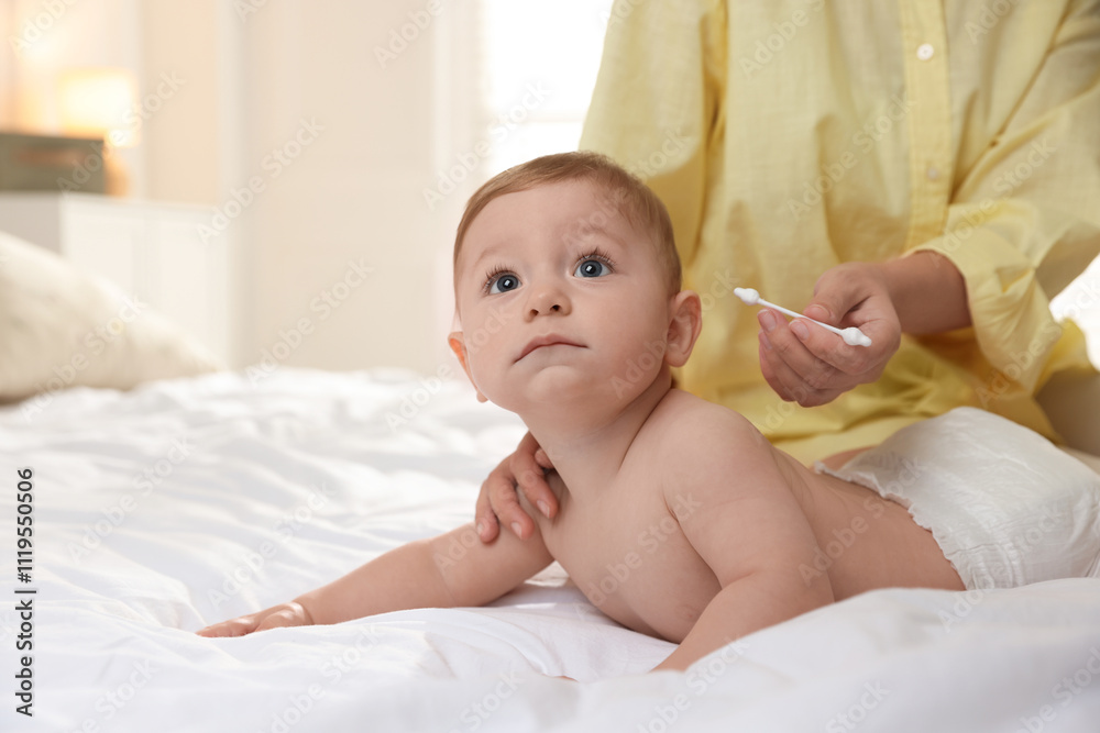 Mother cleaning ear of her cute little baby with cotton swab on bed, closeup Mother cleaning ear of her cute little baby with cotton swab on bed, closeup