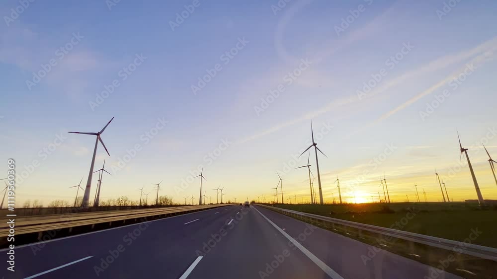 Beautiful sunset on the highway, view from the car. Cars drive along the wide highway, and the sky is colored pink, orange and blue by the setting sun. Many wind turbines rotate on the horizon. Beautiful sunset on the highway, view from the car. Cars drive along the wide highway, and the sky is colored pink, orange and blue by the setting sun. Many wind turbines rotate on the horizon.