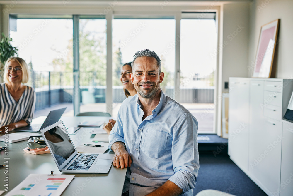 Happy Business Team Meeting in a Modern Office Environment. A mature businessman, with a hint of gray in his hair, wearing a blue shirt, looks directly into the camera. Happy Business Team Meeting in a Modern Office Environment. A mature businessman, with a hint of gray in his hair, wearing a blue shirt, looks directly into the camera.