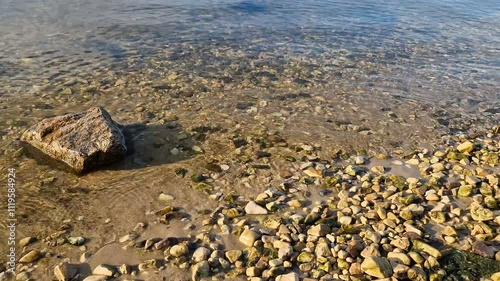 Waves break on the rocks on the beach, sea spray, sunlight is reflected in the water.