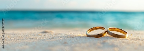 Two gold wedding bands on a white sandy beach with blue ocean in the background. photo