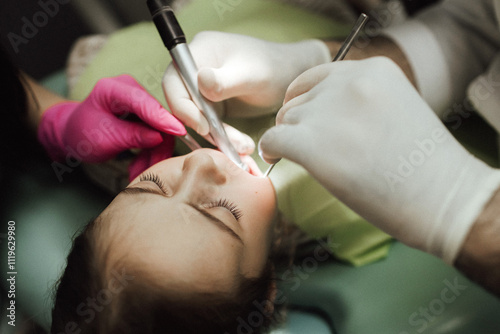 Cropped portrait of little girl with pigtails hair sitting in dental chair looking at camera. A doctor in gloves holds examination tools. Children's dentistry. Part of a series photo