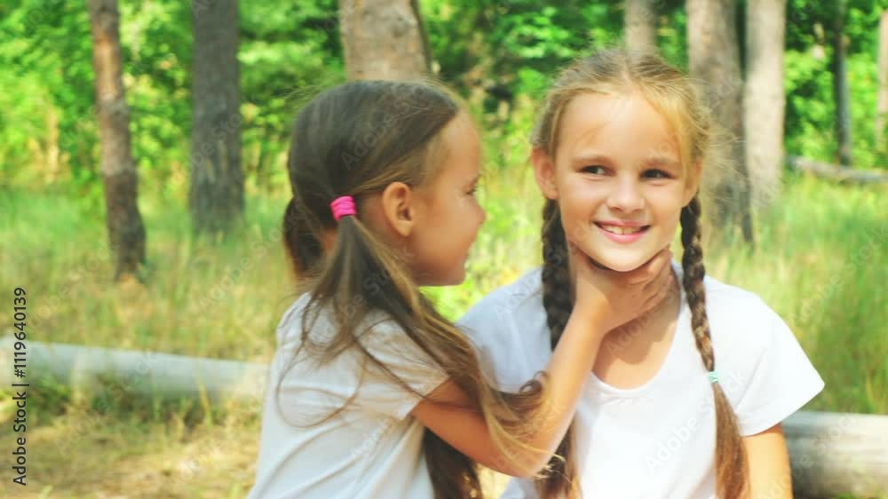 Two children little sisters sit on top of a huge, fallen log indicating the surrounding area, having fun at a summer camp Two children little sisters sit on top of a huge, fallen log indicating the surrounding area, having fun at a summer camp