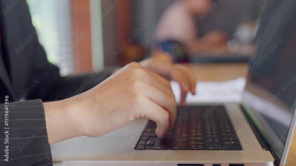 A person is typing on a laptop computer. The laptop is on a table and the person is wearing a suit