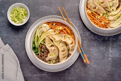 Food photography of soup ramen with vegetable gyoza dumplings, soba, buckwheat noodles, spring onion, carrot, Bok choy, chopsticks; vegan food, Chinese and Japanese cuisine