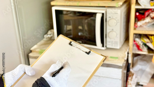 Foto 電子レンジ前でクリップボードに記入する軍手をはめた手