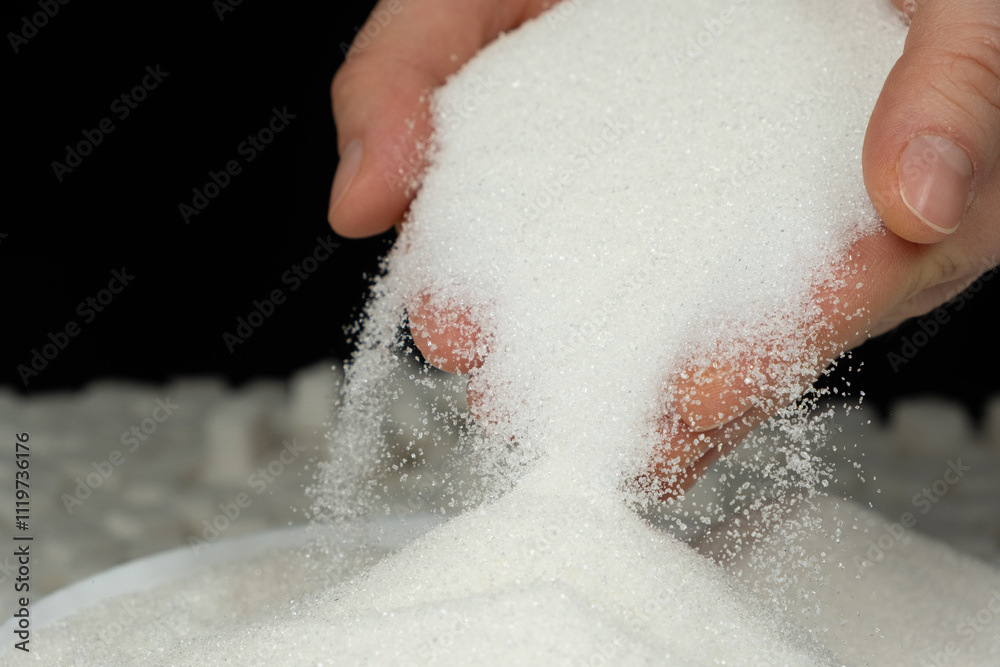 Hands pouring white crystalline refined sugar, black background Hands pouring white crystalline refined sugar, black background