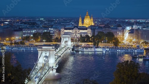 Budapest, Hungary - The famous Szechenyi Chain Bridge (Lanchid) and St. Stephen's Basilica at night, with street lights glowing on the Danube River, capturing the city's night charm
