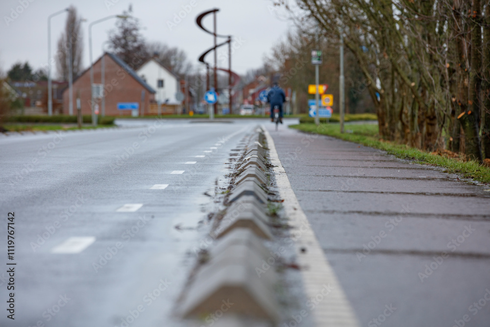 City street with bike lane, marked by concrete barriers, on a wet day. Residential buildings in the background. City street with bike lane, marked by concrete barriers, on a wet day. Residential buildings in the background.