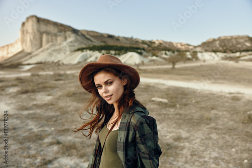 Woman in plaid shirt and hat standing in field with mountains in background on sunny day photo