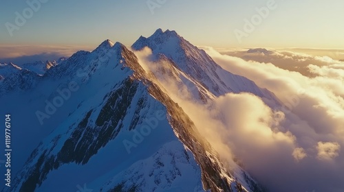 Aerial view of majestic mountains surrounded by stunning snow-covered peaks and dramatic clouds during sunset