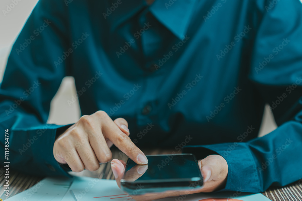 person in blue shirt using smartphone while sitting at table, focused on screen. setting suggests casual or professional environment