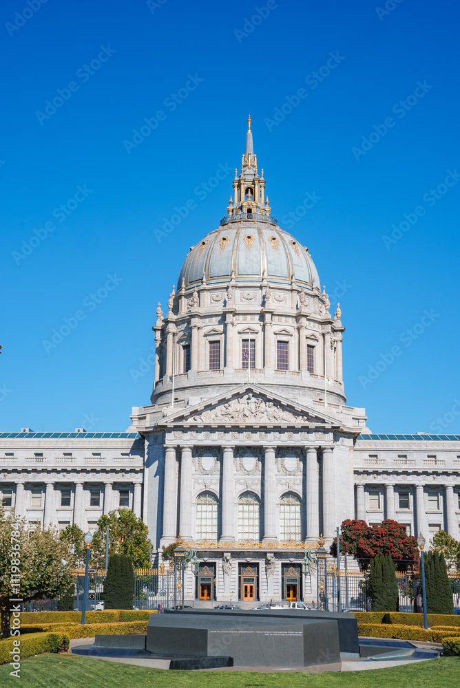 Obraz premium San Francisco City Hall stands with its grand dome and intricate facade under a clear blue sky, surrounded by gardens and pathways in the civic center.