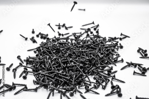 A small pile of black screws on a white background. Fastening materials for fastening drywall structures