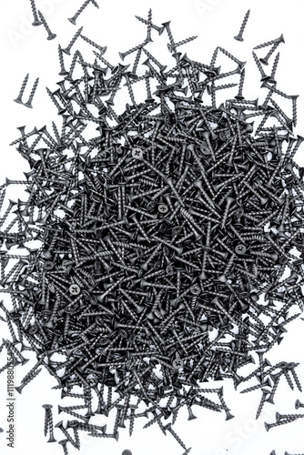 A small pile of black screws on a white background. Fastening materials for fastening drywall structures