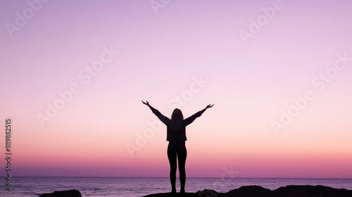 Woman raising outstretched arms to the pink sky at sunset over the ocean