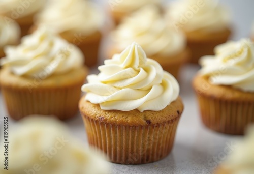 Close-up of golden-brown cupcakes with white frosting on light gray surface