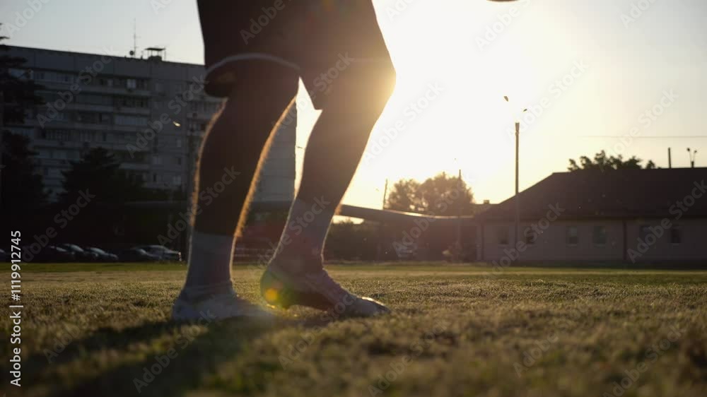Legs of young man kicking ball at green field. Male feet of professional footballer juggling soccer ball on stadium at sunset. Sportsman practicing tricks outdoor. Concept of a freestyle football