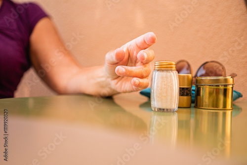 Close-Up of Hand Reaching for Salt Shaker on Table Beside Metal Containers and Sunglasses in Outdoor Setting