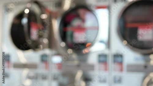 Close-up view of laundromat dryers captures vibrant reflections and blurred details, evoking sense of everyday life and bustling atmosphere of shared laundry spaces