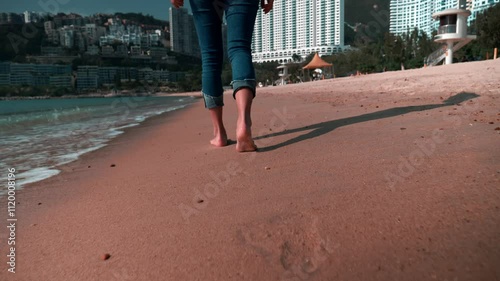 Legs of a beautiful young sporty woman in rolled-up jeans walking along the Hong Kong beach in sunshine