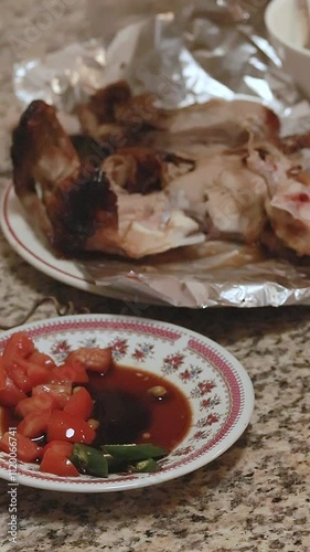 Dipping lechon manok in spicy sawsawan and eating it with raw tomatoes with bare hands that shows a candid and authentic Filipino cultural cuisine photo