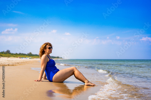 Beautiful middle aged woman sitting and sunbathing on sea shore in summertime. Side view