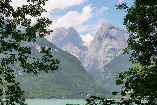 Tree branches framing majestic mountain peak Croz Dell'Altissimo in pristine Brenta Dolomites, National Park Adamello Brenta, Trentino, Italy. Wanderlust at calm alpine lake Lago di Molveno in summer photo