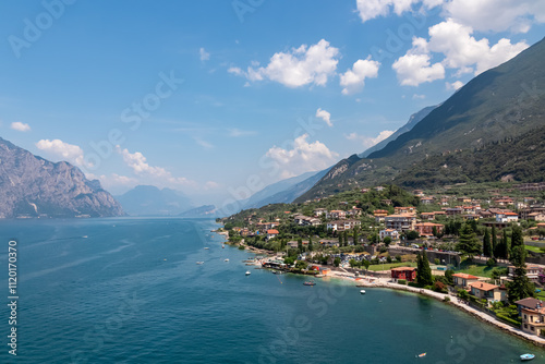 Aerial view of idyllic coastline of Lake Garda seen from viewing platform Rivellino of Scaliger Castle, Malcesine, Veneto, Italy. Surrounded by rugged mountains and cliffs of Garda Hills. Summer vibe