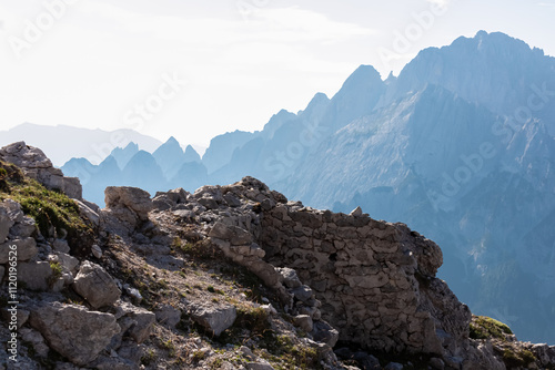 Hiking trail along remains of defensive line first world war on top of Jof di Miezegnot. Surrounded by majestic ridges of Julian Alps shrouded in misty haze, Friuli Venezia Giulia, Italy. Wanderlust photo