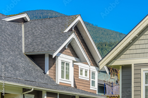 Top of grey stucco luxury house with shingle roof, red and yellow trees and nice windows in Summer in Vancouver, Canada, North America. Day time on June 2024.