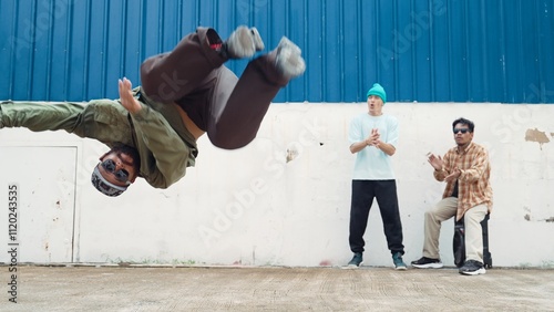 Tableau sur toile Asian hipster doing somersault in front of wall with lively friend