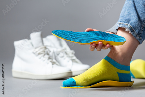 Close up of female hands holding blue orthopedic insoles, white sneakers on a gray background .