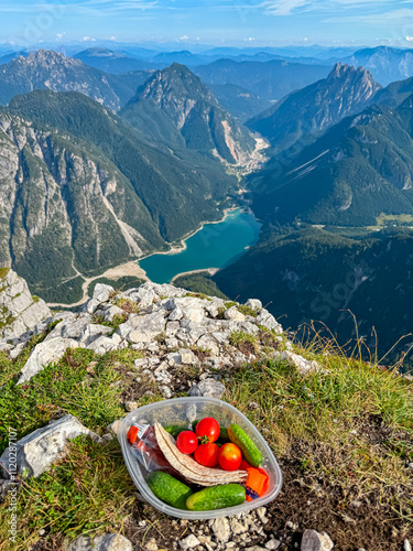 Eating healthy snack on top of Cima Del Lago with aerial view of alpine lake Lago Del Predil. Val Canale surrounded by majestic mountain peaks of Julian Alps, Friuli Venezia Giulia, Italy. Wanderlust photo