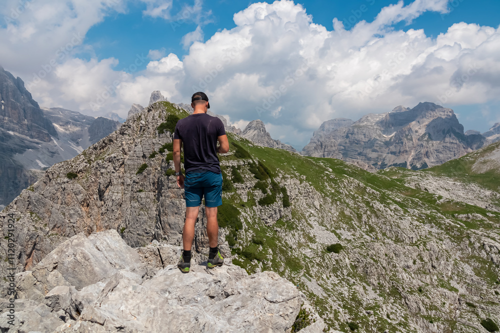 Hiker man on top of Croz dell'Altissimo with panoramic view of majestic cloud covered rugged mountain peaks of Brenta Dolomites, Trentino, Italy. Summer wanderlust in alpine wilderness Italian Alps Hiker man on top of Croz dell'Altissimo with panoramic view of majestic cloud covered rugged mountain peaks of Brenta Dolomites, Trentino, Italy. Summer wanderlust in alpine wilderness Italian Alps